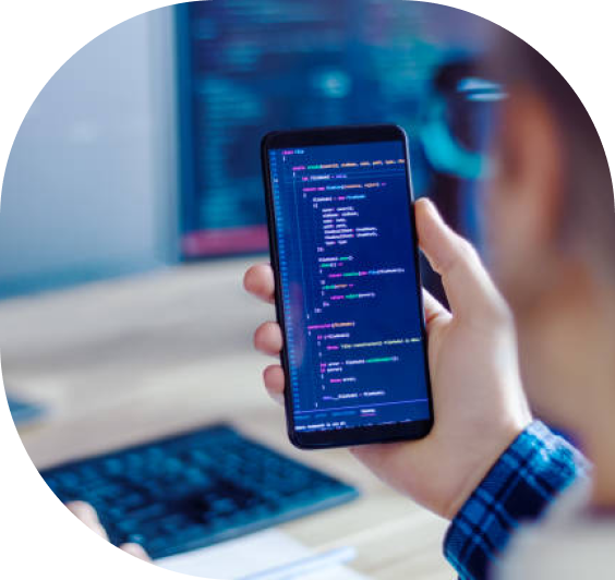 Close-up of developer analyzing code on a smartphone with desktop coding setup in the background, demonstrating mobile-first development.