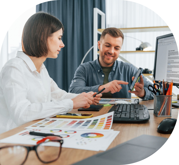 Creative designers discussing color palettes and mobile app layout at a desk with printed charts and digital design tools