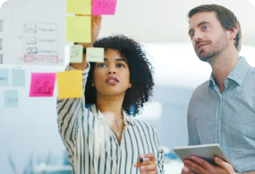 Two colleagues collaborating with sticky notes on a whiteboard during a UX design brainstorming session.