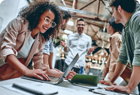 Diverse group of young professionals brainstorming around a laptop in a modern office, representing teamwork and collaborative innovation.