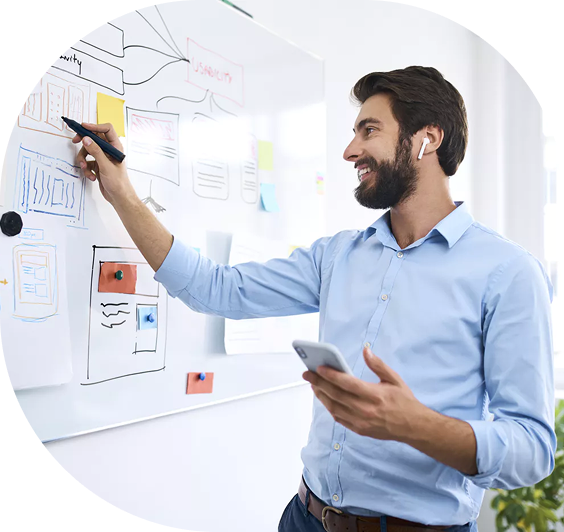 Male UX designer presenting wireframes and user flow on a whiteboard, using a marker and smartphone in a bright office setting.